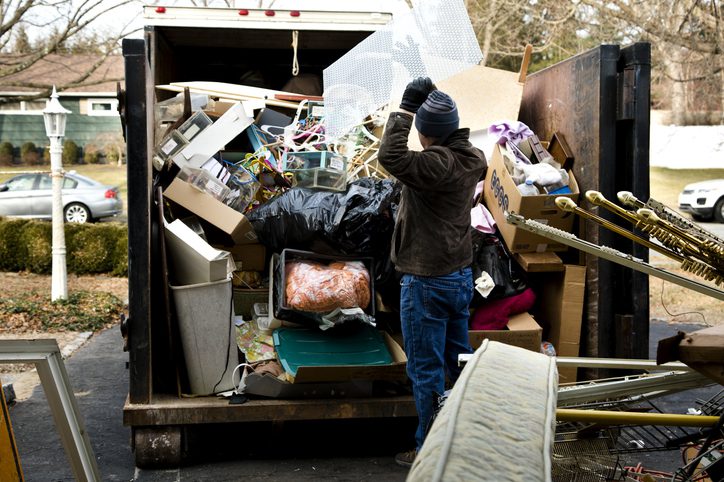 A person sorting through a large dumpster filled with various discarded items in an outdoor setting.