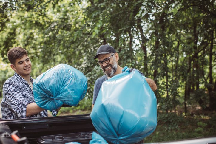A man loading blue trash bags into a vehicle outdoors.