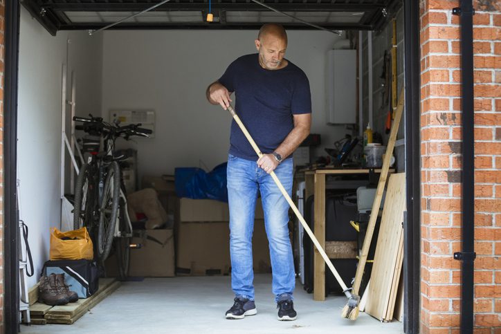Man sweeping the floor in a garage or workshop space.