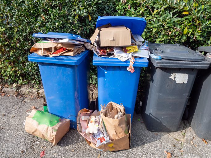 Overflowing garbage bins with trash spilling out onto the ground outdoors.
