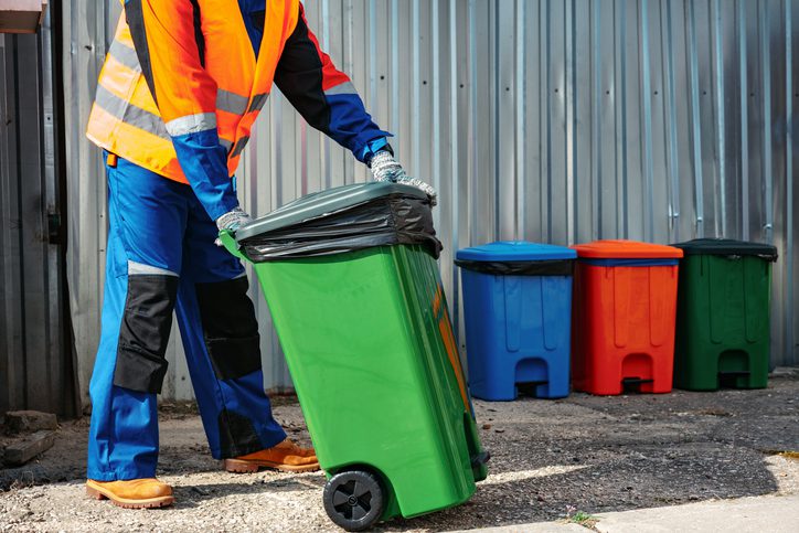 Male janitor in uniform cleans a trash can in the street close up