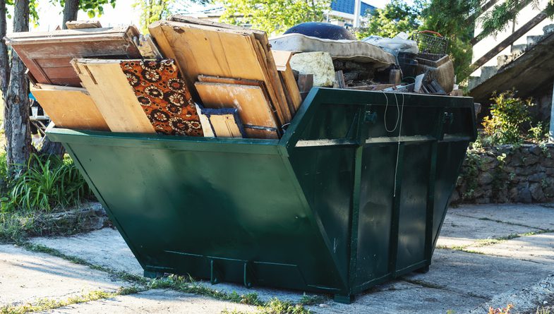 A green dumpster filled with furniture and household items outdoors.