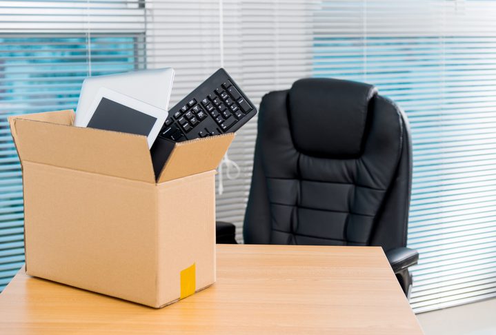 Box with office supplies on an empty desk and chair.