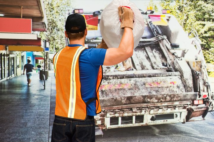 Worker loading garbage into a truck wearing safety vest.