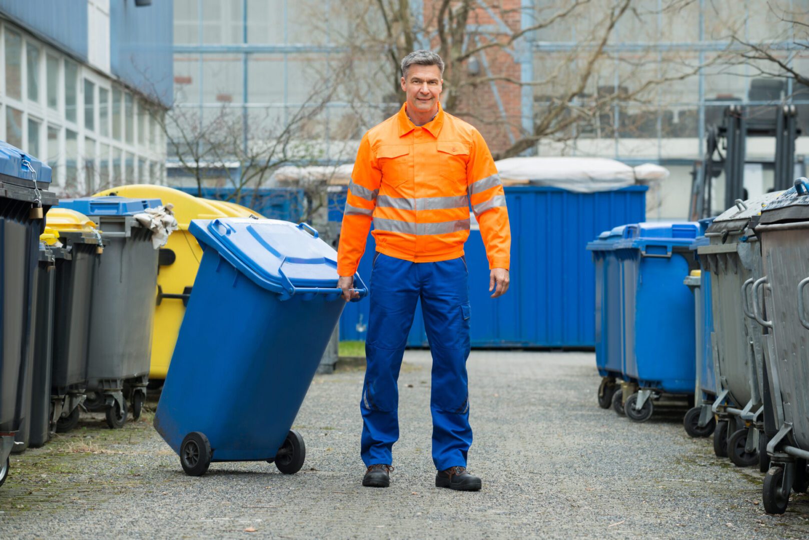 Happy Male Worker Walking With Dustbin On Street During Day