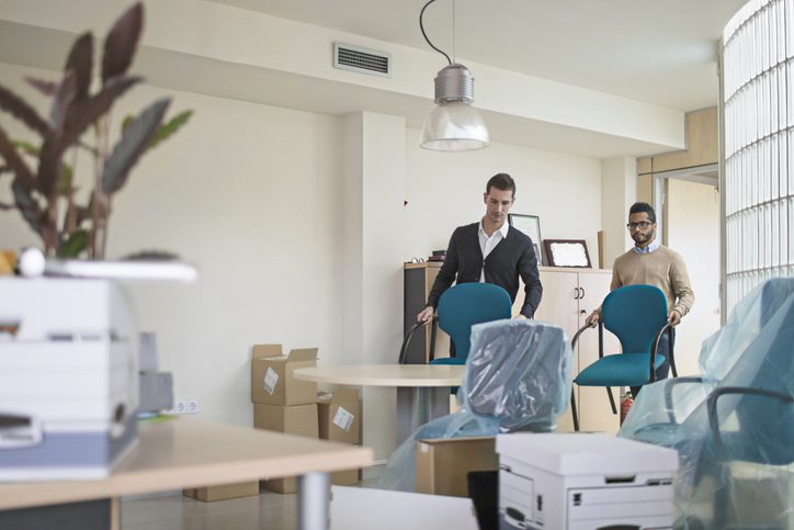Two men setting up a new office space with furniture and boxes.